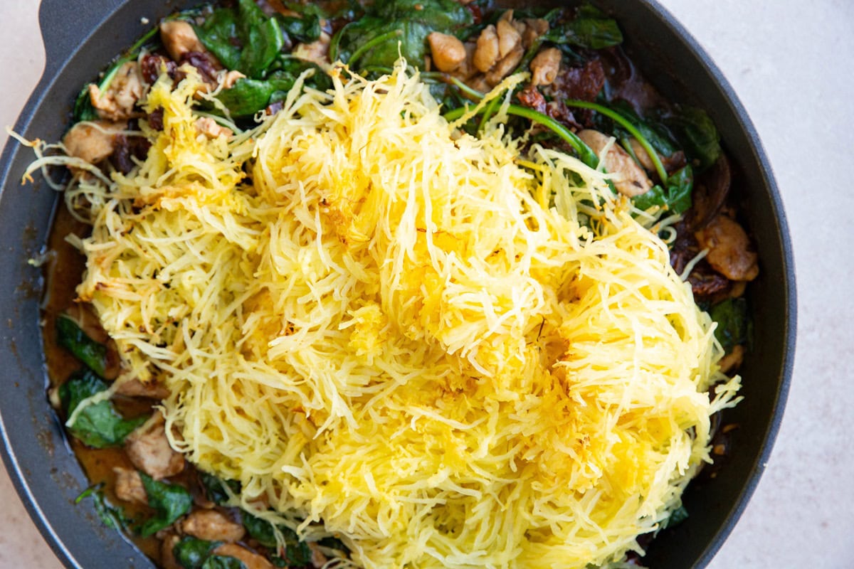 Spaghetti squash on top of sun-dried tomato mixture, ready to be mixed in.