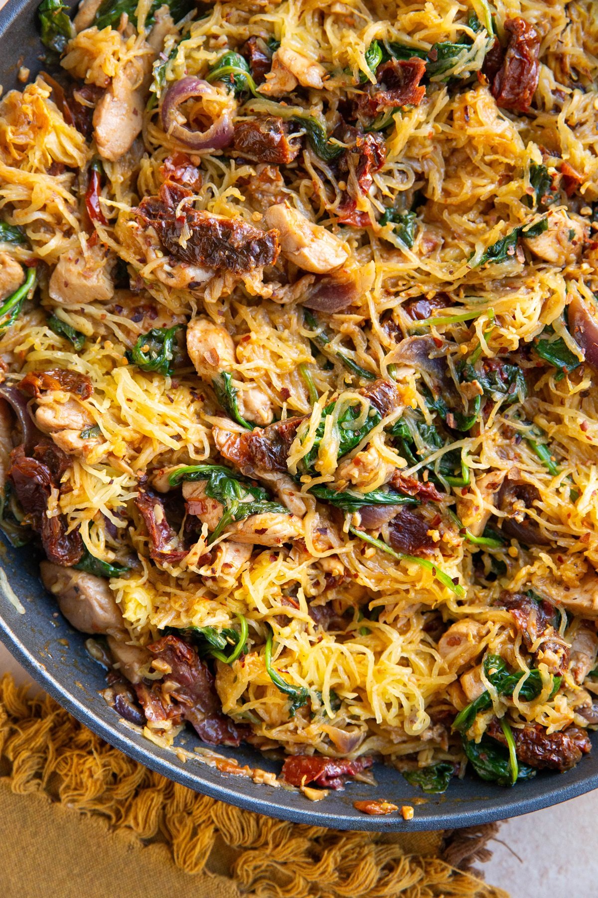 Sun-dried tomato spaghetti squash finished in a skillet, ready to serve and a napkin to the side.