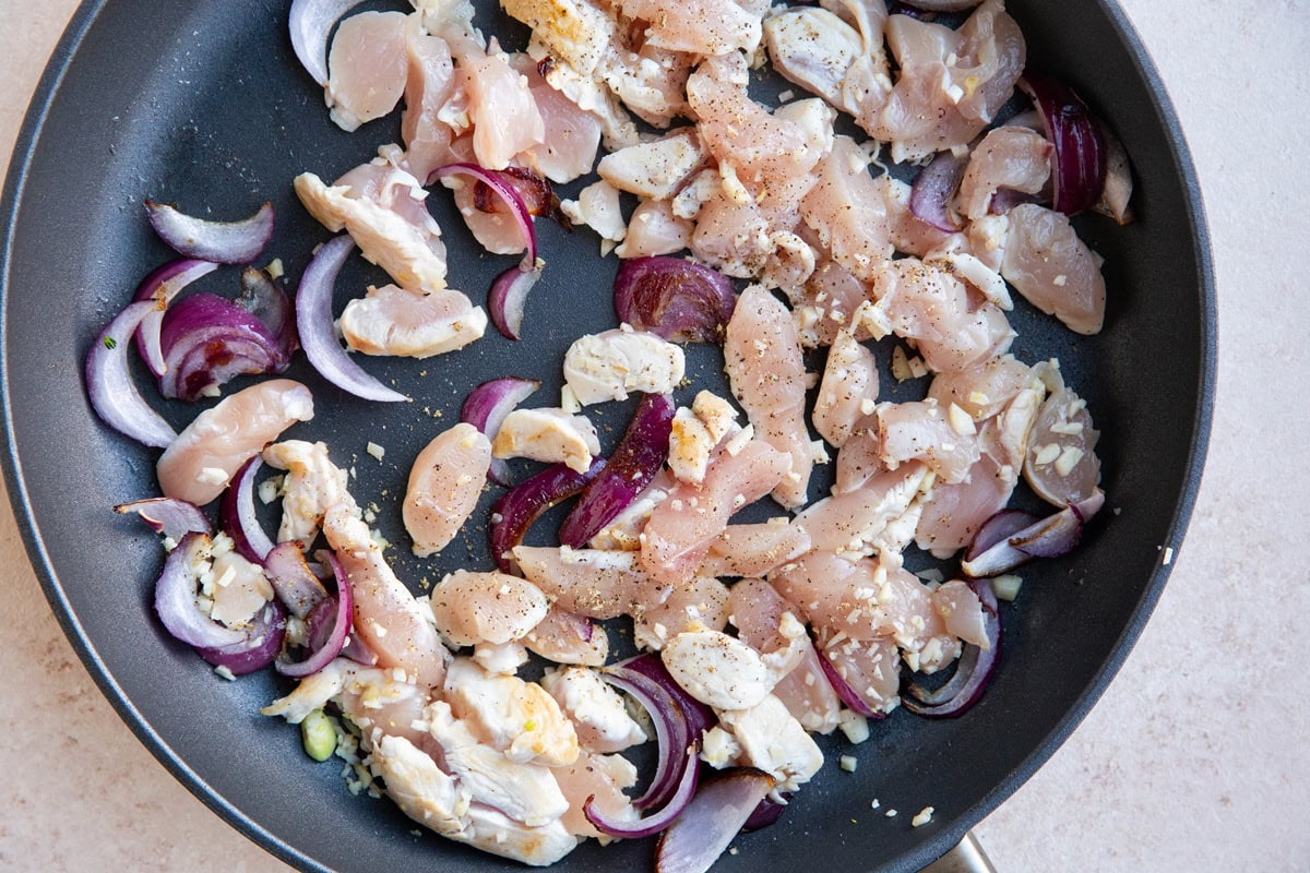 Onion, garlic, and chicken cooking in a skillet.