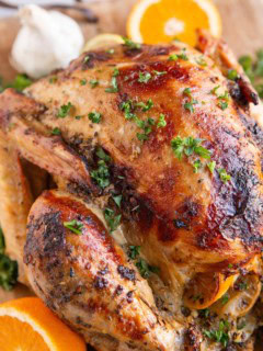 Whole roast turkey on a wooden cutting board with sliced oranges and fresh garlic in the background.