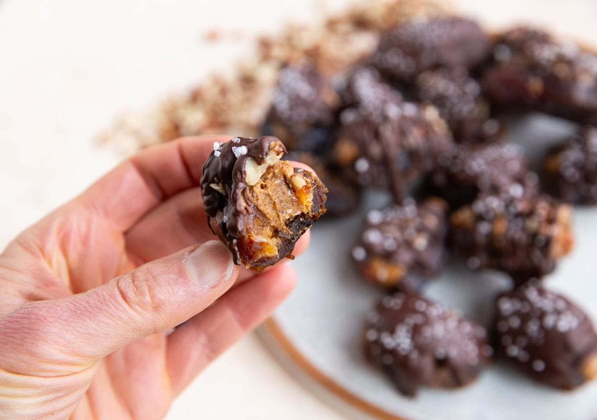 Hand holding a date with a bite taken out of it.