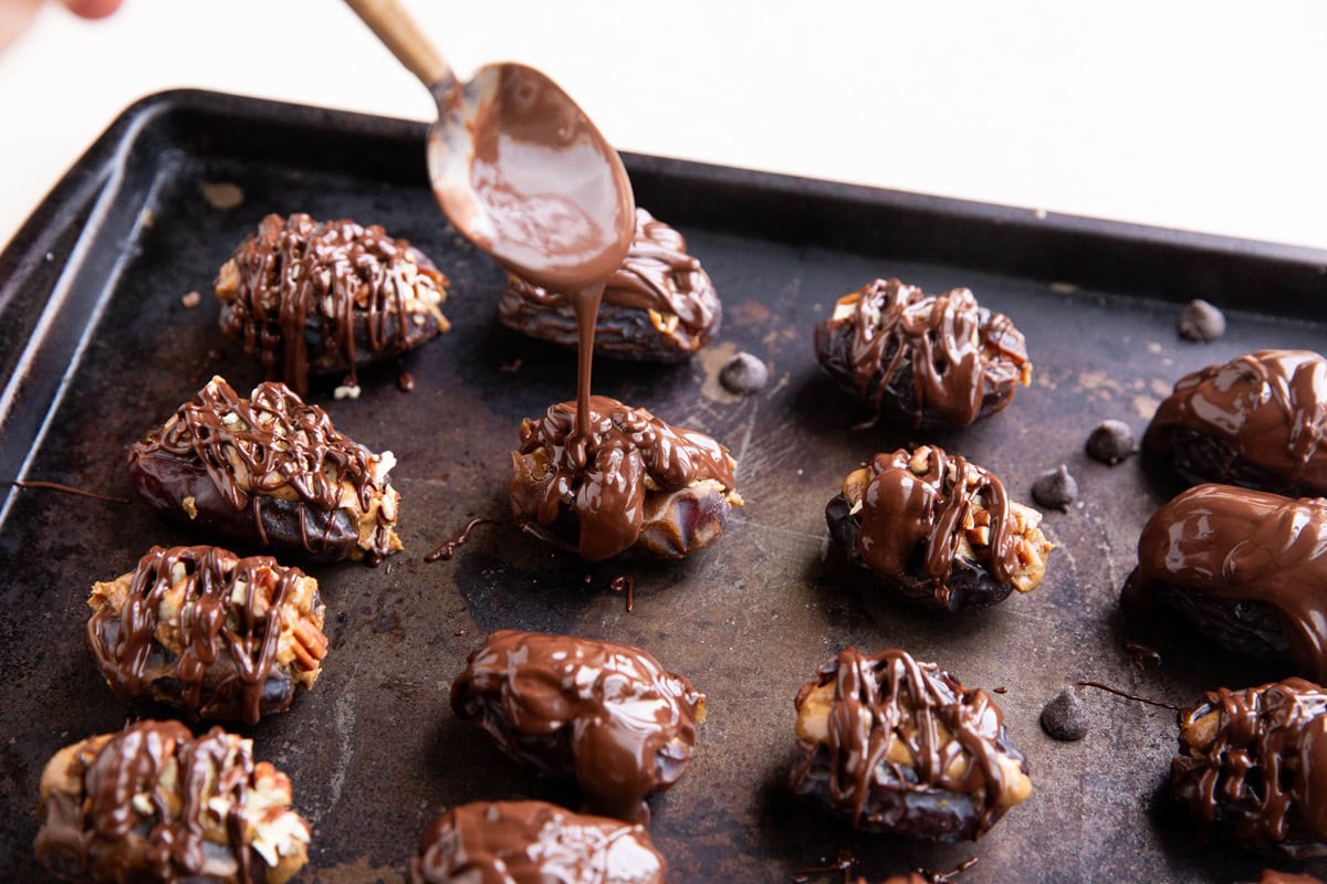 Spoon drizzling melted chocolate over stuffed dates.