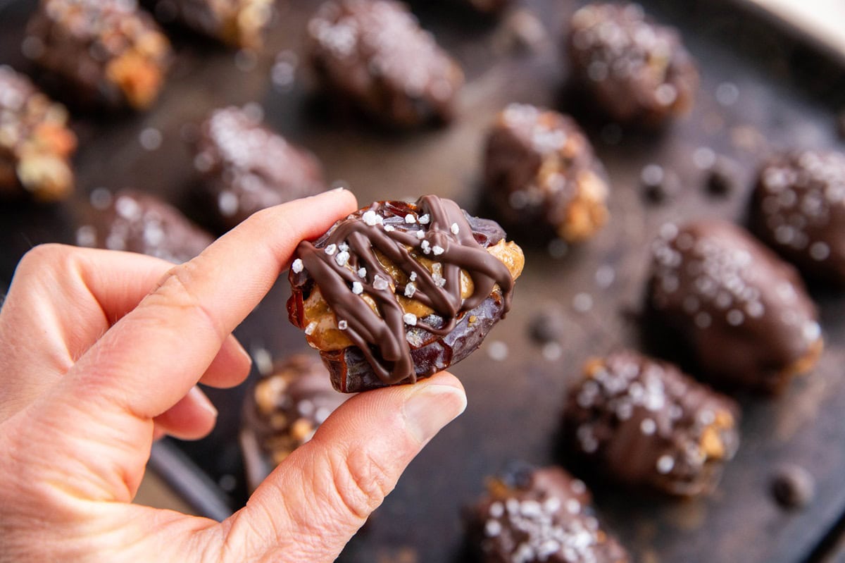 Hand holding a chocolate covered almond butter stuffed date.