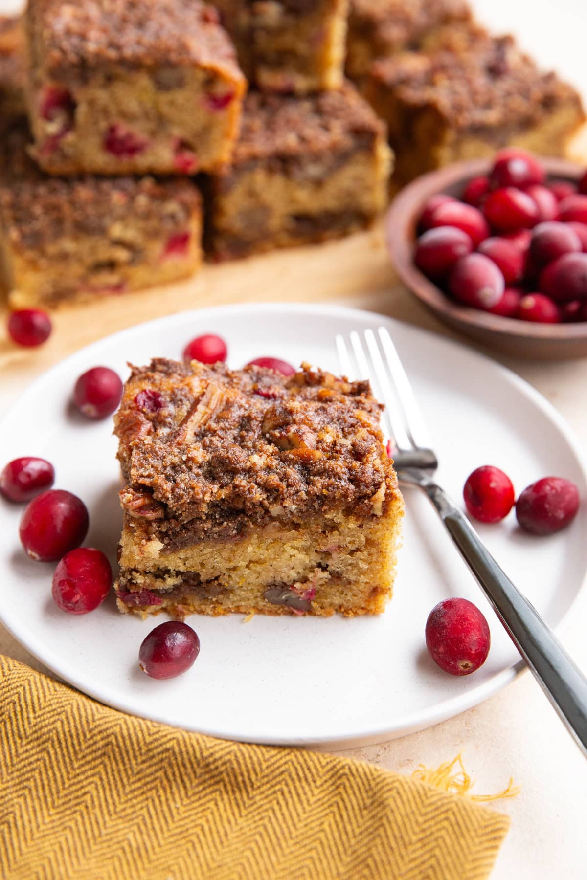 Slice of cranberry orange cake on a white plate with the rest of the cake in the background.