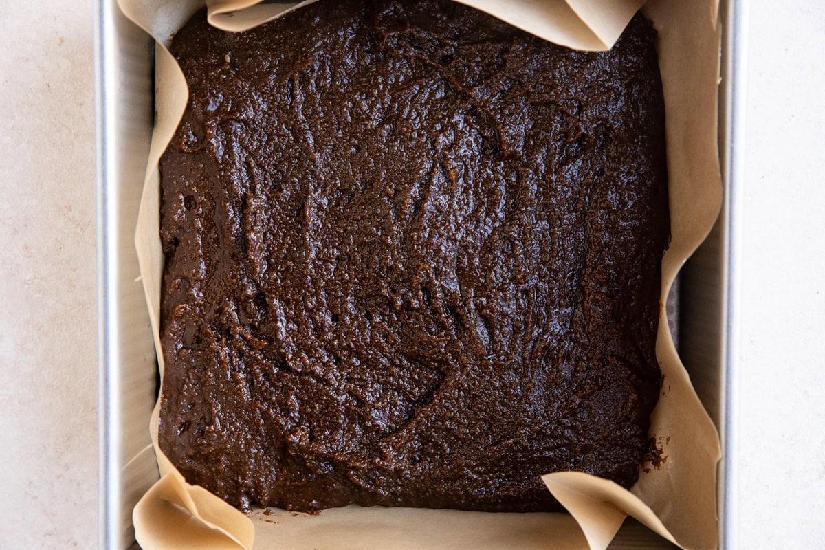 Gingerbread cake batter in a square baking pan, ready to go into the oven.