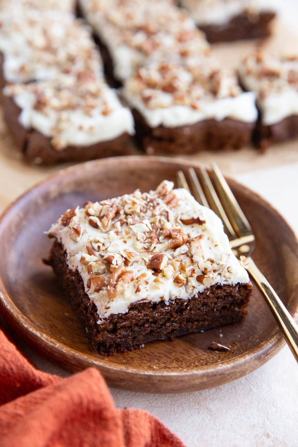 Slice of cake on a wooden plate with the rest of the cake in the background.