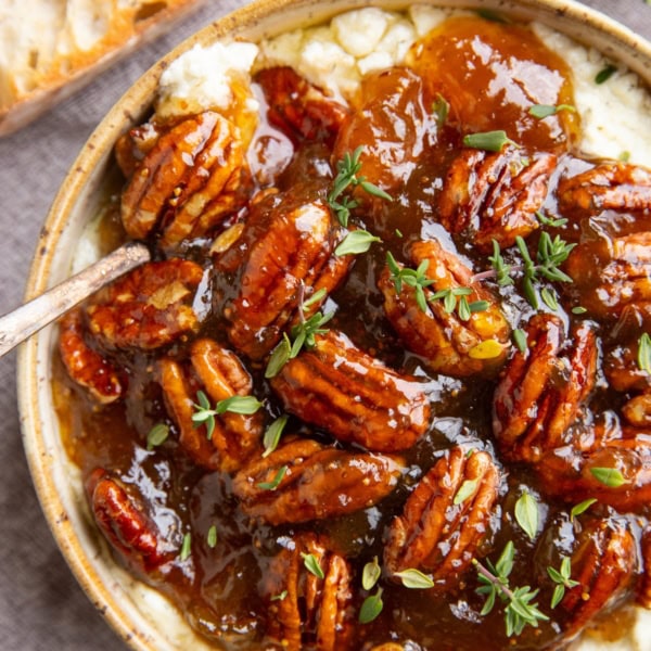 Baked feta dip in a ceramic bowl with fig jam and pecans on top, ready to serve.