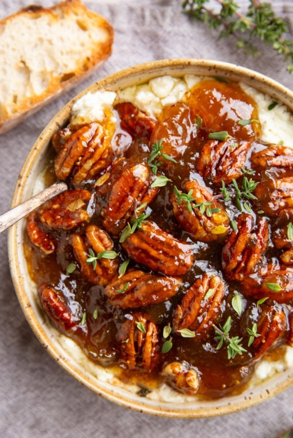 Baked feta dip in a ceramic bowl with fig jam and pecans on top, ready to serve.