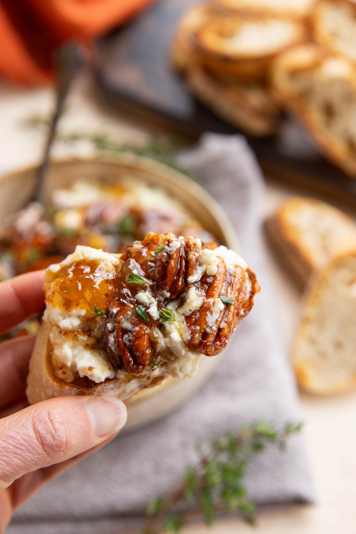Hand holding a crostini with creamy baked feta and pecans spread on top.