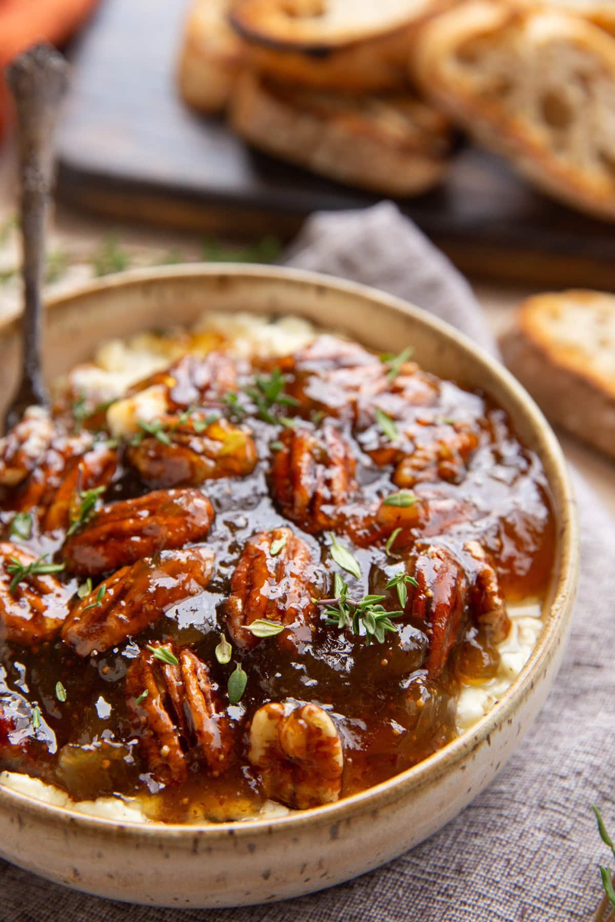 Bowl of baked feta cheese with fig jam and pecans on top.