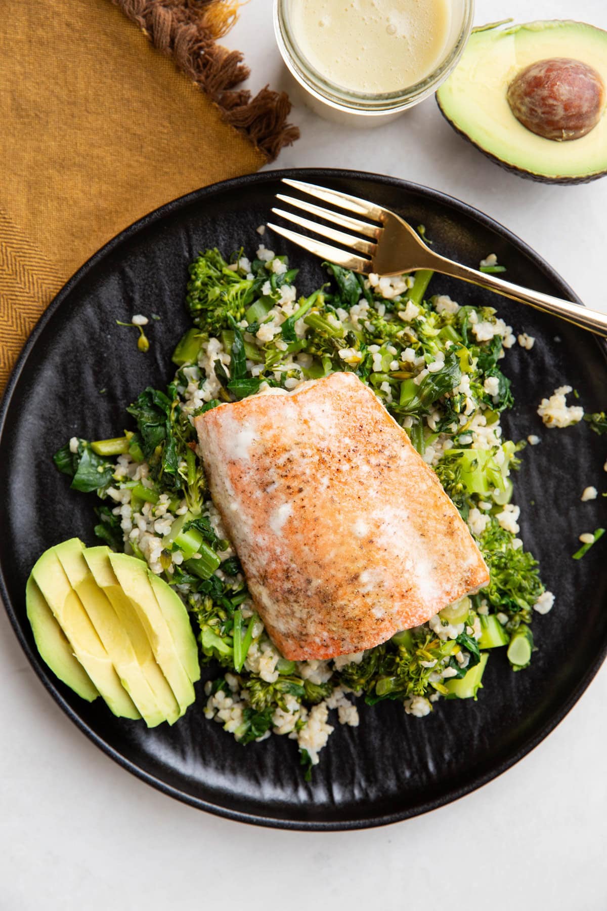 Salmon on top of rice and veggies with avocado on a black plate, ready to eat.