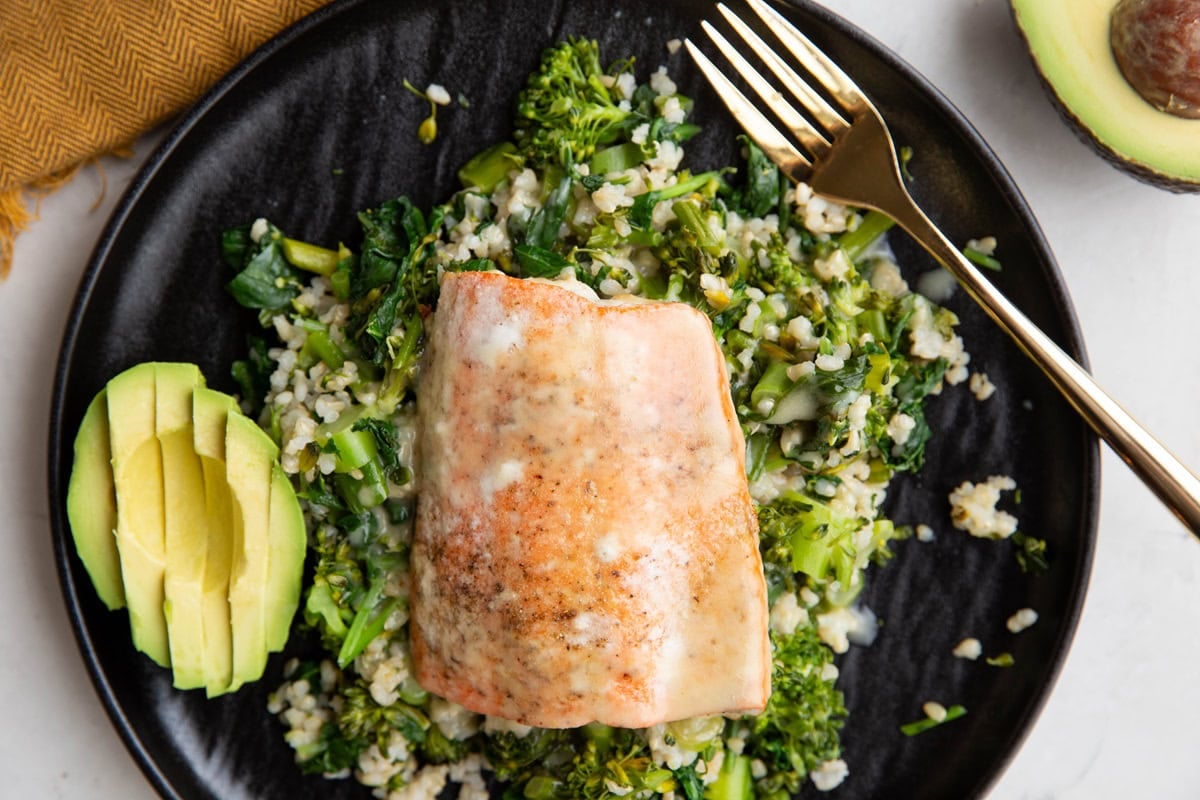 Sockeye salmon with dressing on top on top of rice and veggies with sliced avocado.