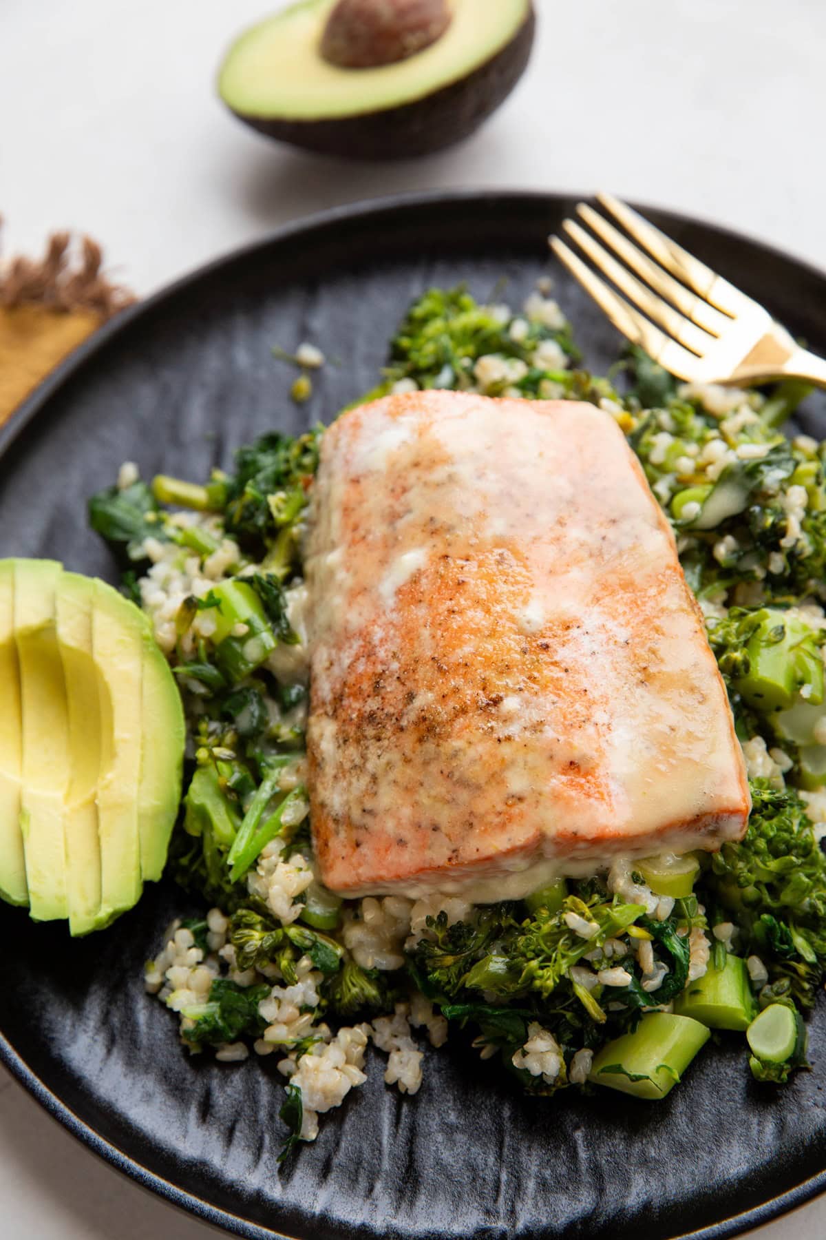 Sockeye salmon on a black plate with rice, broccoli, and spinach with sliced avocado to the side.