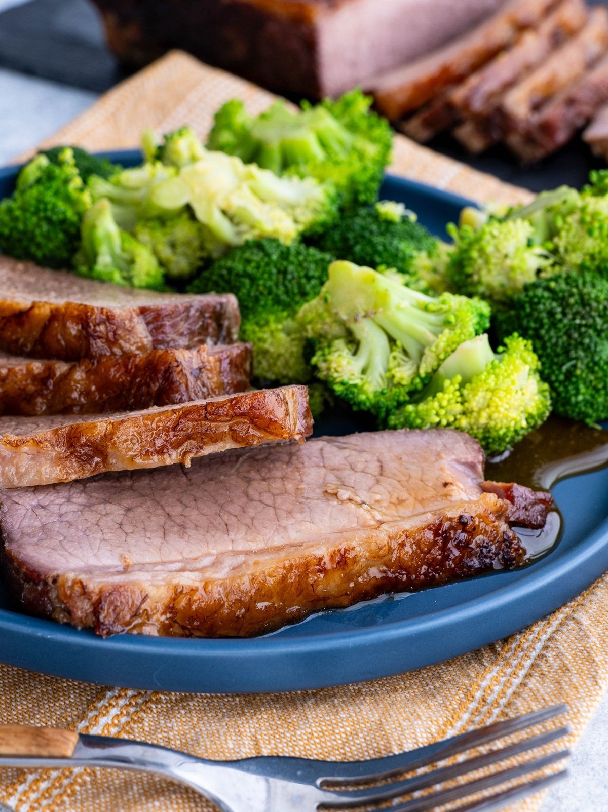 Blue plate of thin slices of brisket with steamed broccoli to the side.