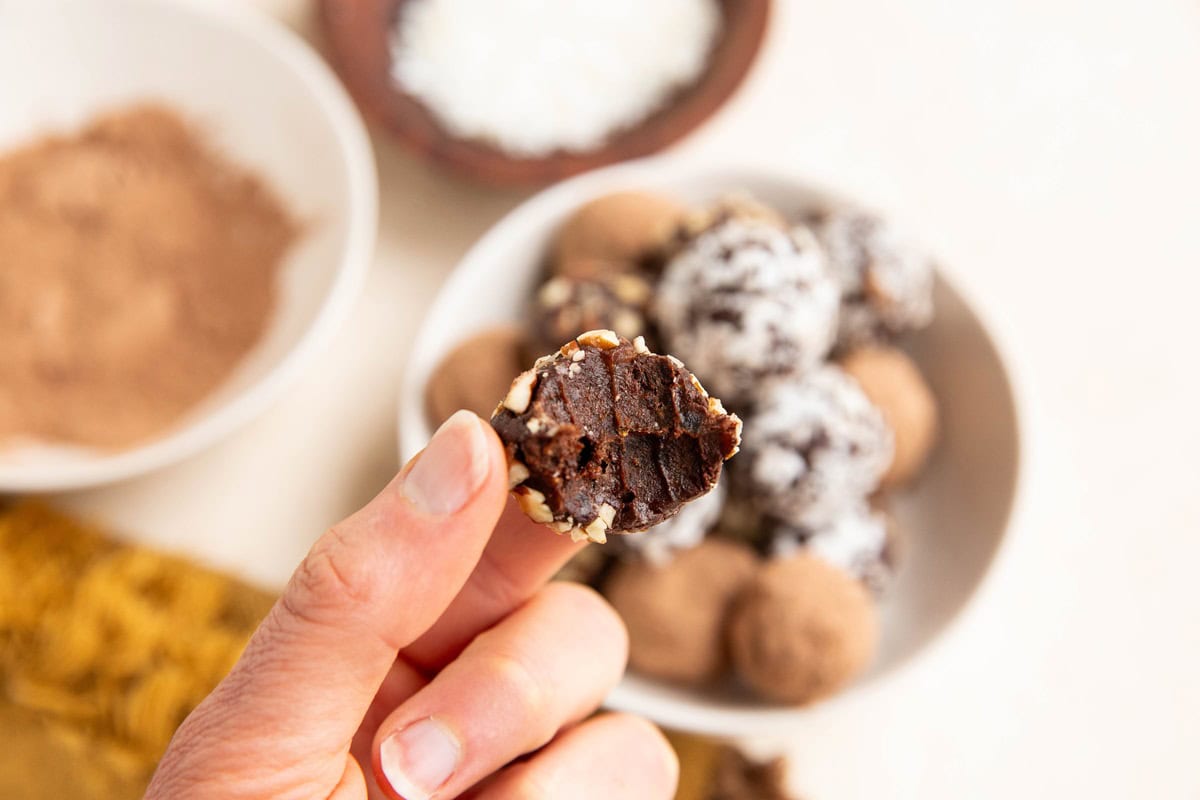 Hand holding a chocolate truffle with a bite taken out.