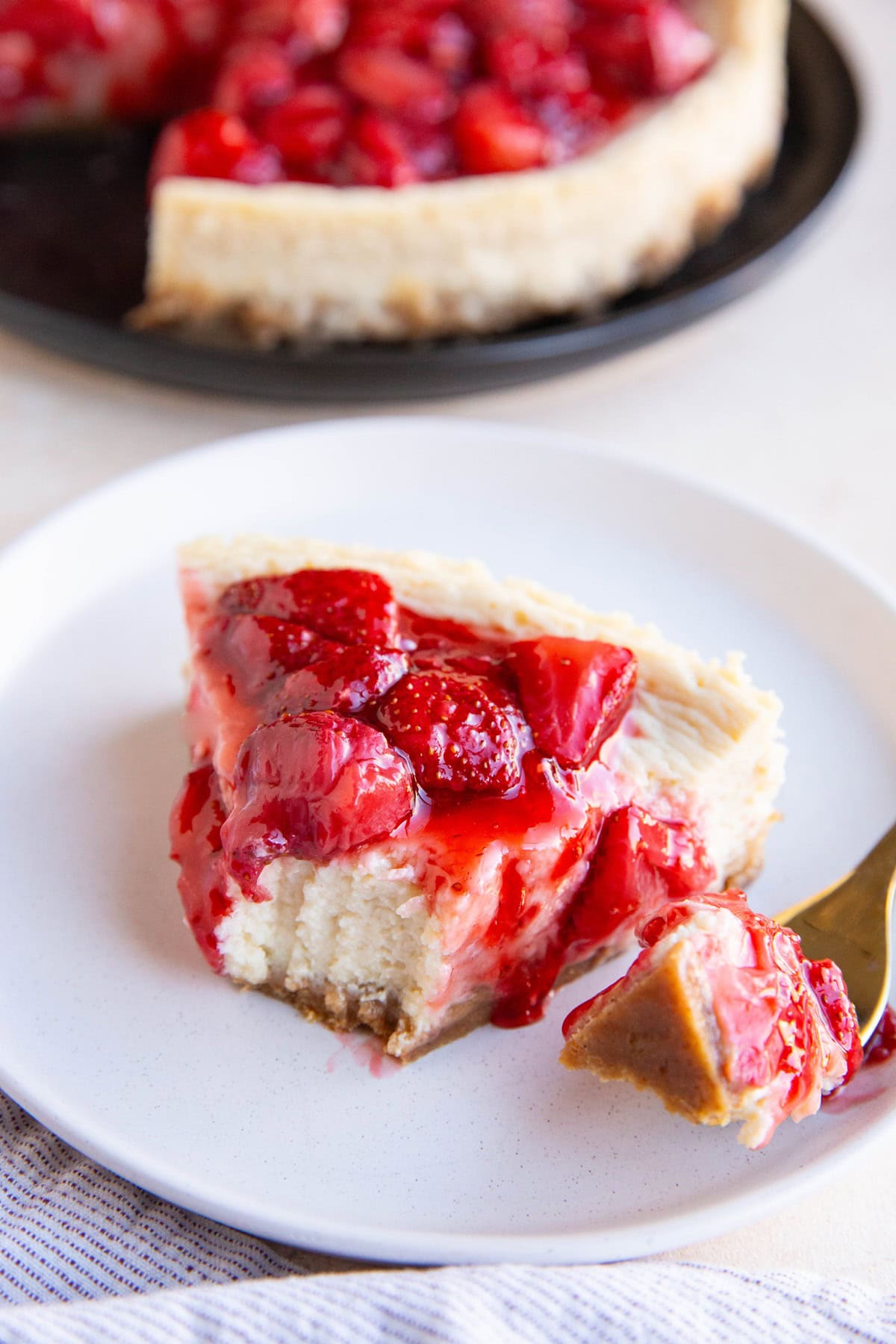 Slice of cottage cheesecake on a white plate with a bite taken out.