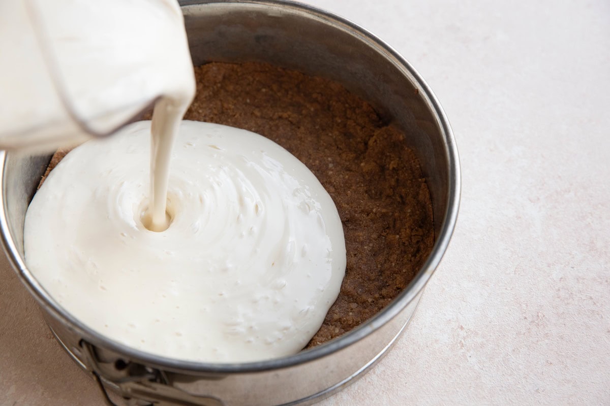 Pouring cheesecake filling over the pre-baked pie crust.