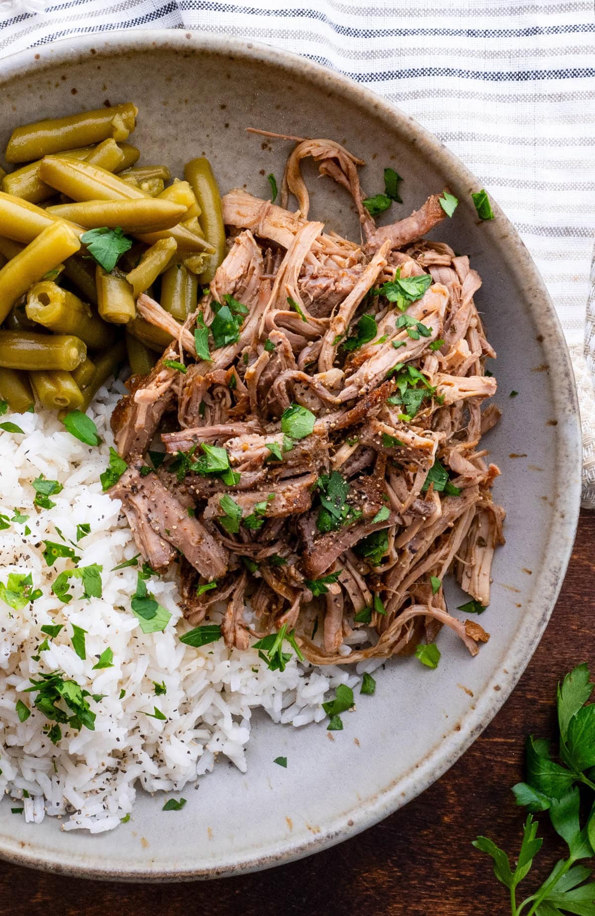 Bowl full of rice, green beans, and pulled pork, garnished with parsley.