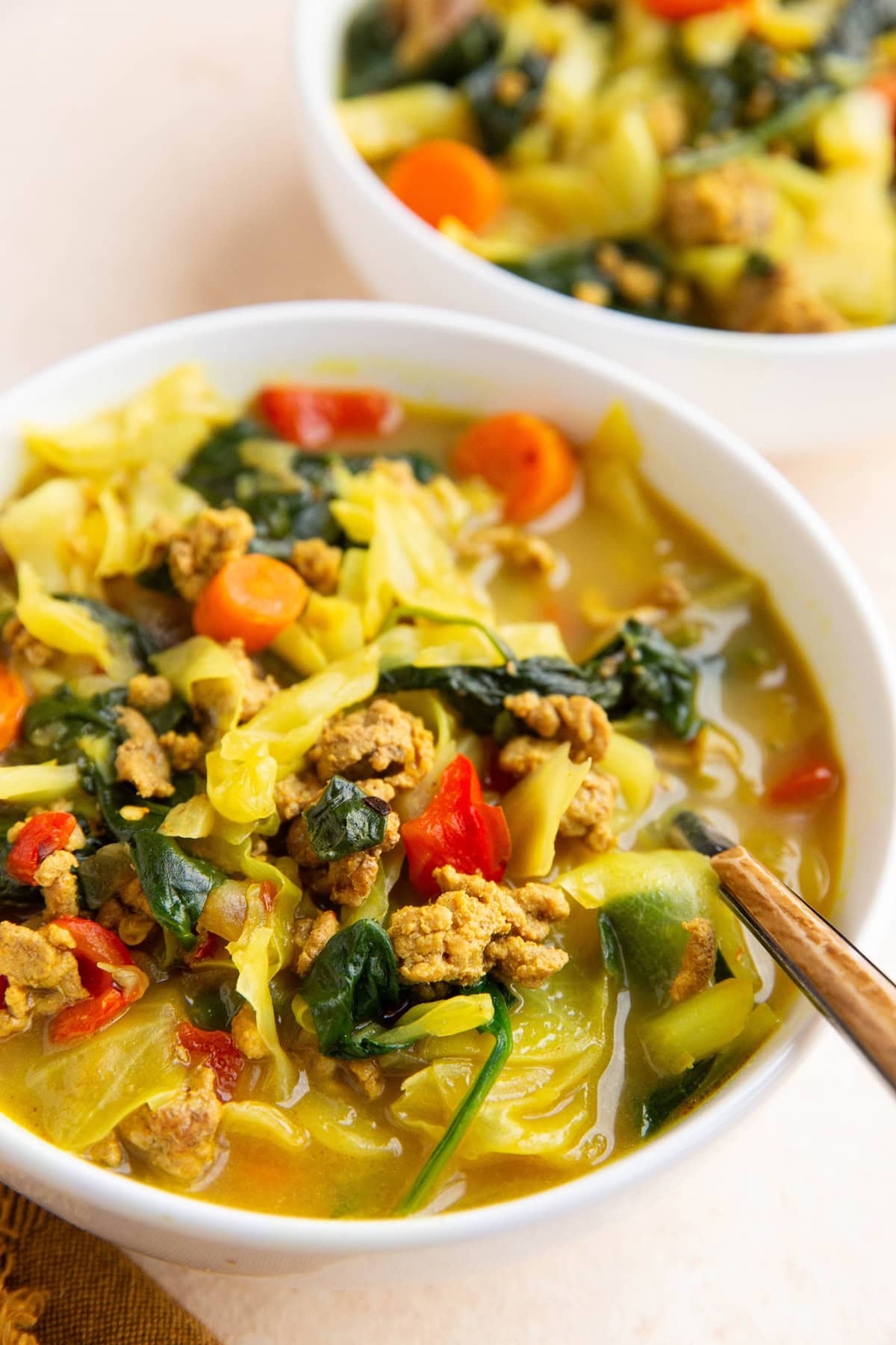 Two white bowls of curry ground turkey cabbage soup.