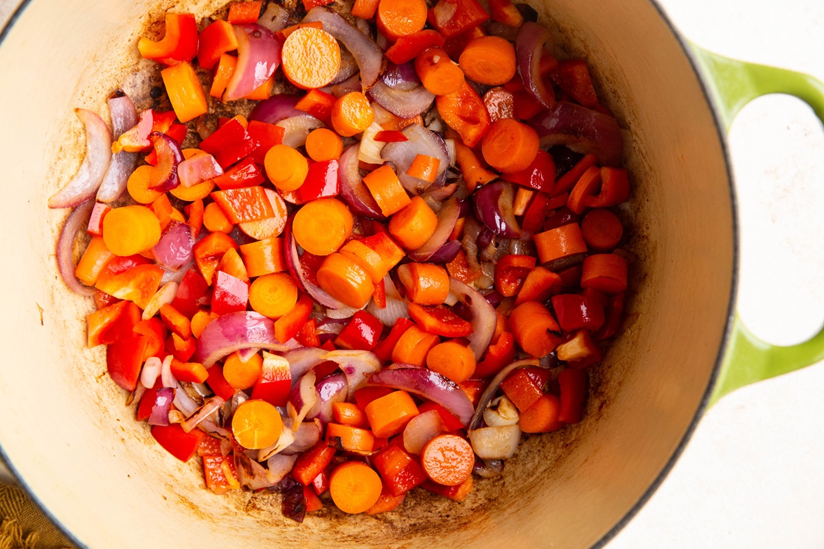 Carrots, onions, and bell peppers cooking in a large pot.