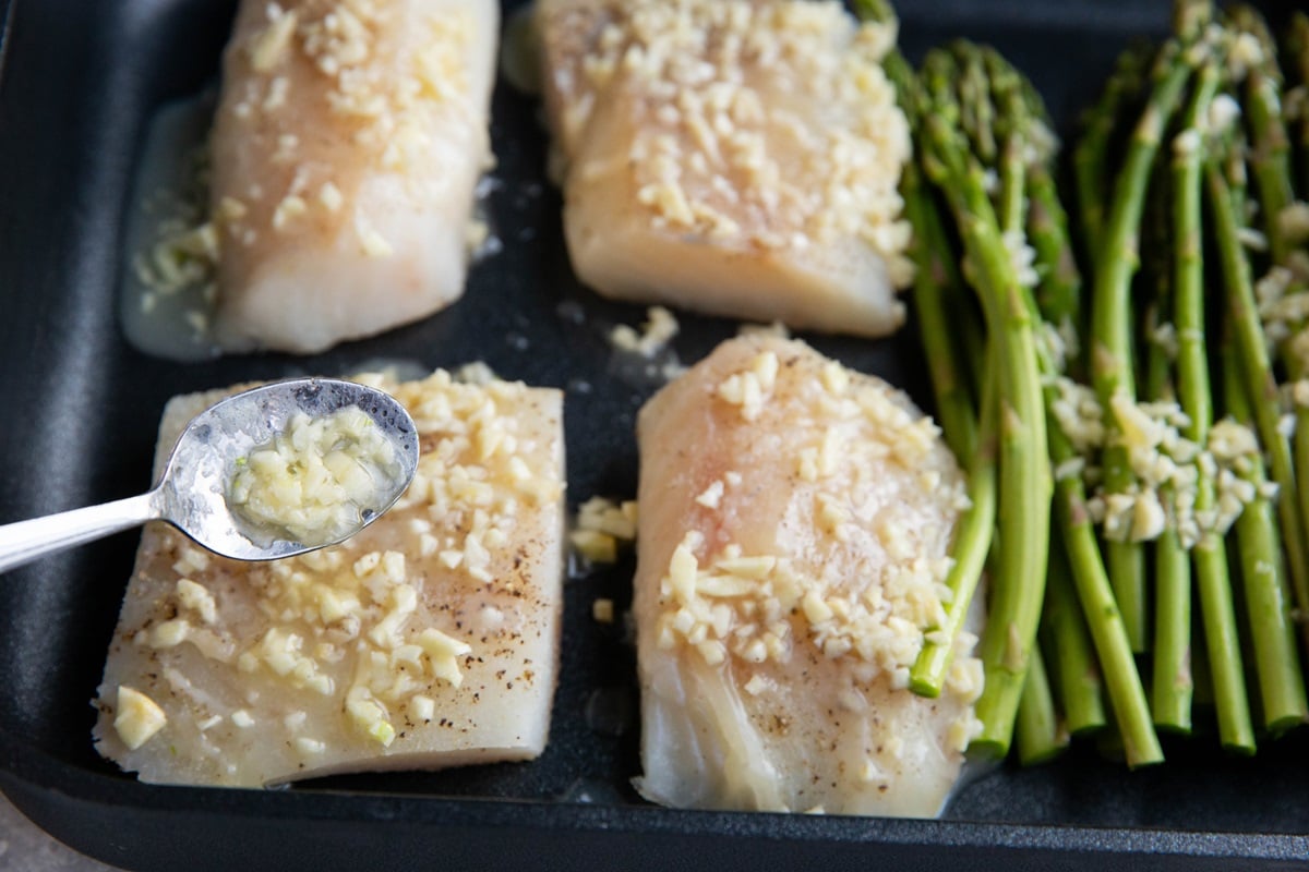 Cod fillets in a baking dish being drizzled with garlic butter sauce.
