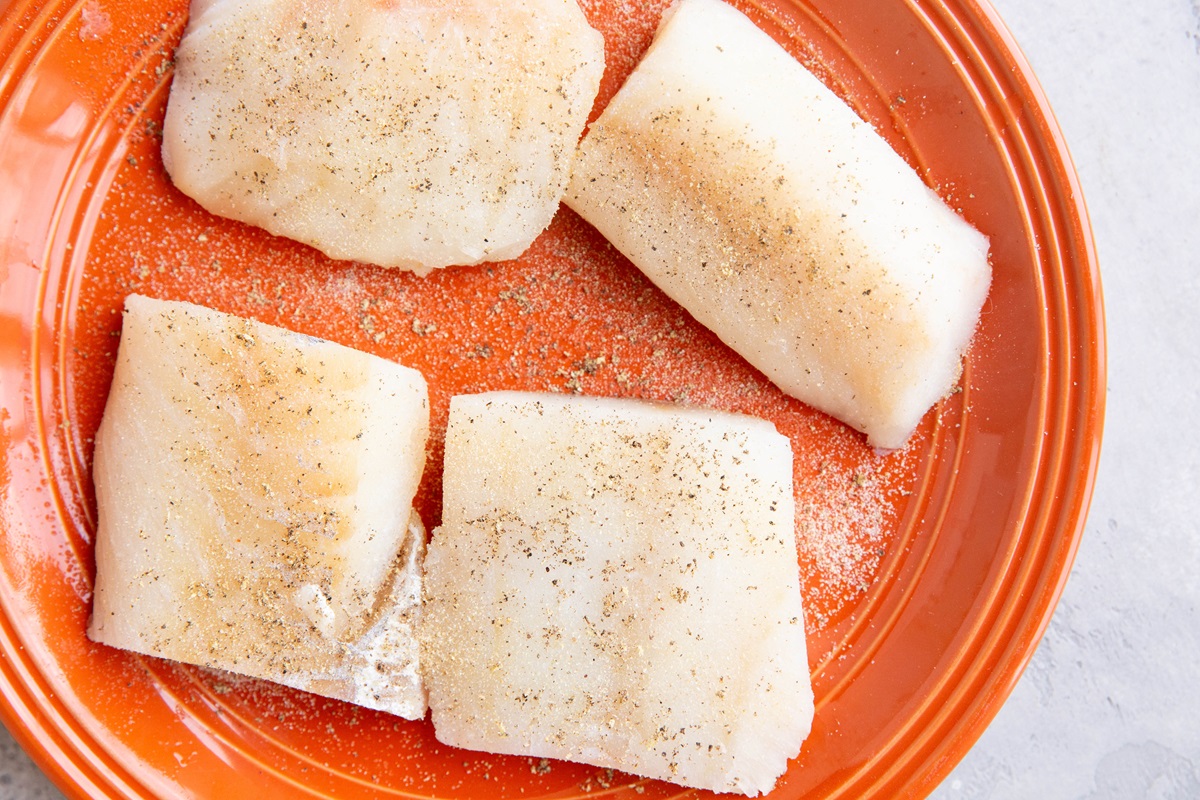Cod filets on a plate, seasoned with salt, pepper, and garlic powder.