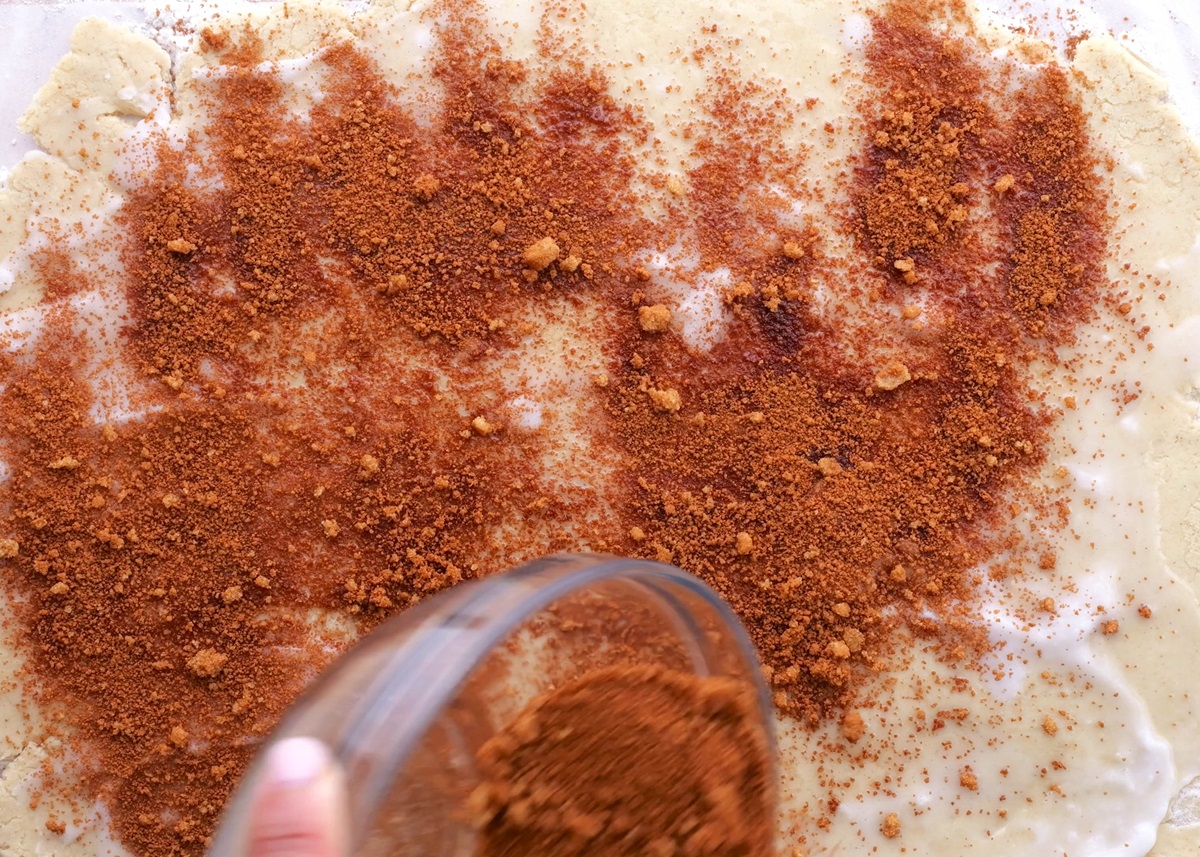 Cinnamon roll dough being sprinkled with cinnamon and sugar.