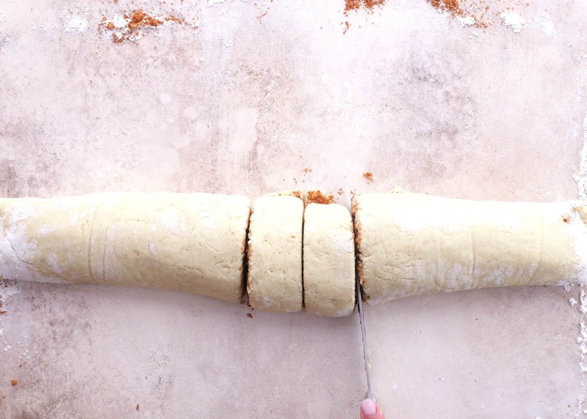 Cinnamon roll dough being cut with a knife into dough rounds.