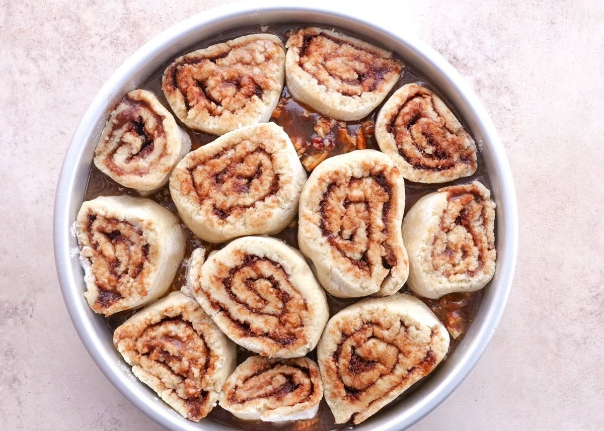 Raw cinnamon roll dough in a cake pan on top of caramel sauce.