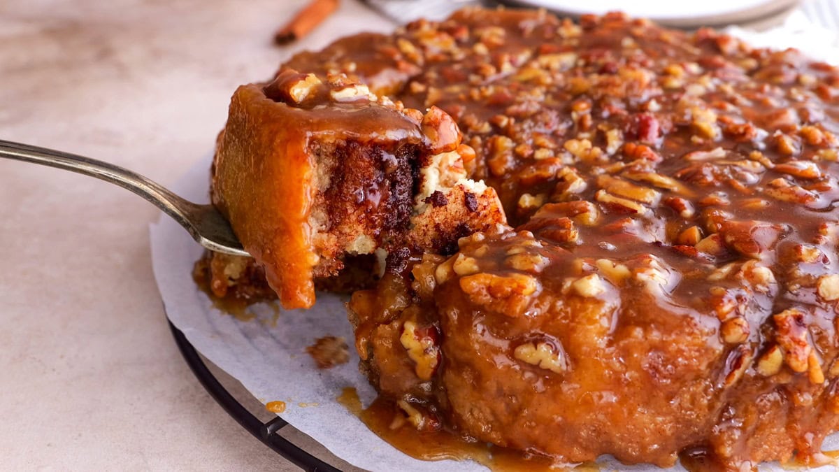 Fork pulling off a cinnamon roll from the mass.