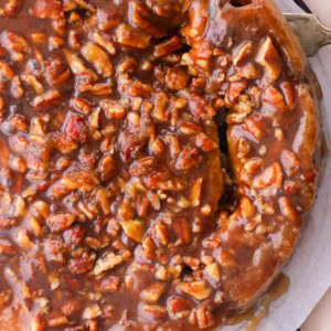 Full batch of pecan sticky buns on a serving plate with a fork taking one out.