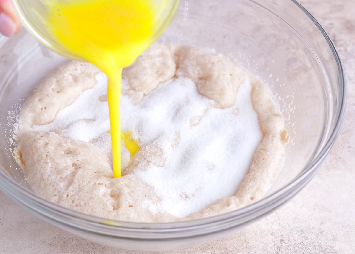 Yeast in a bowl with sugar sprinkled on top and beaten egg being mixed in.