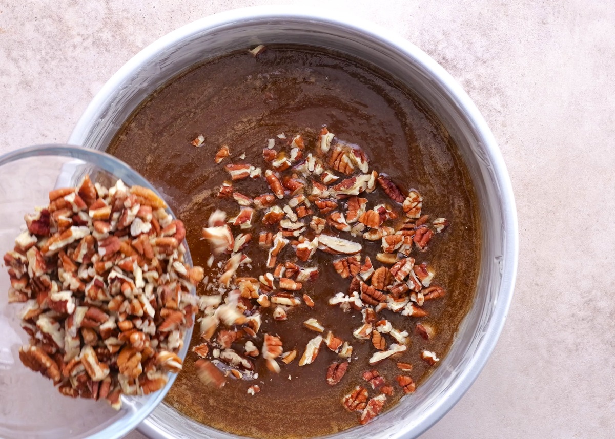 Caramel at the bottom of a greased pan with pecans being sprinkled on top.