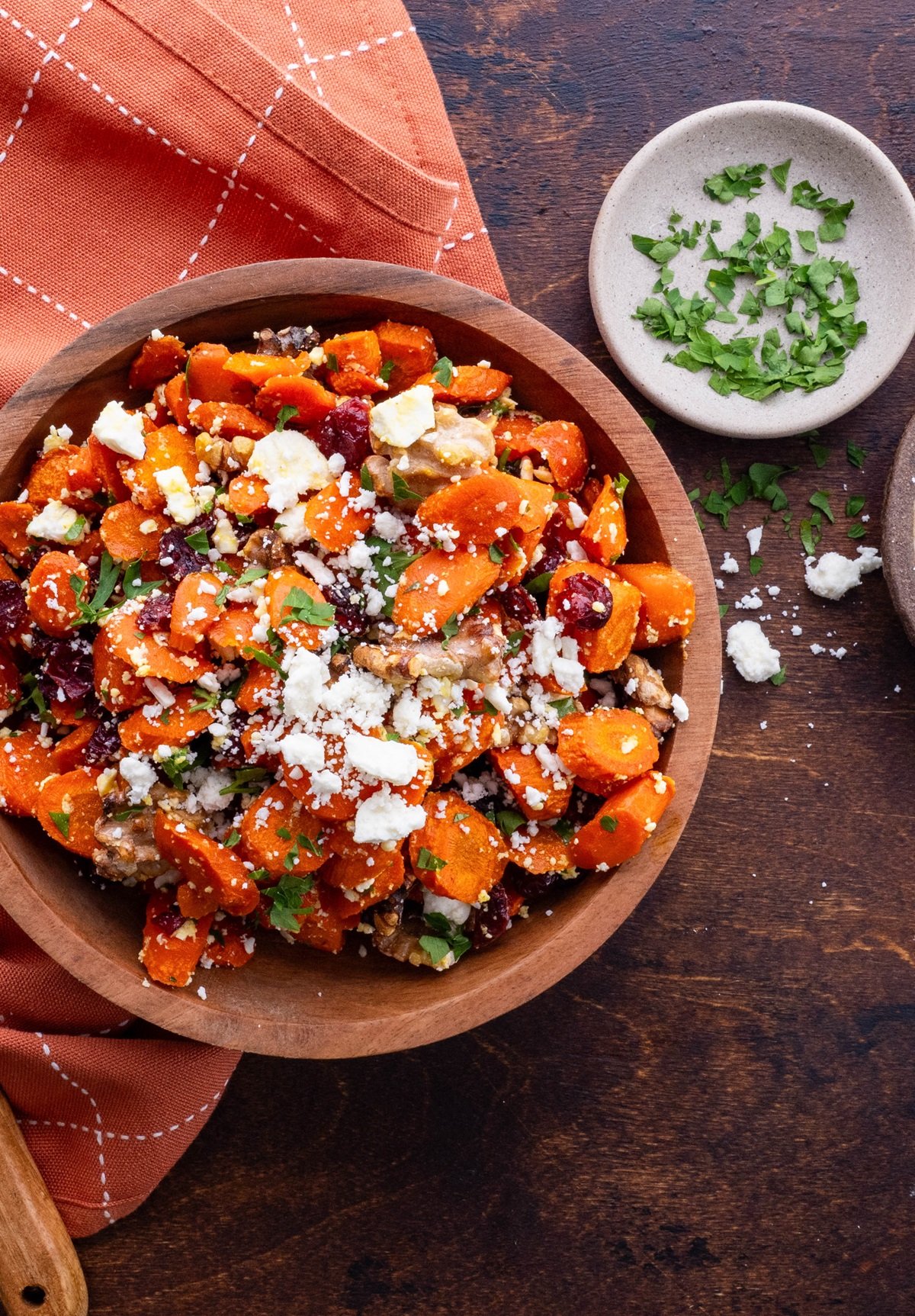Wooden bowl with roasted carrots inside topped with feta, cranberries, and walnuts.