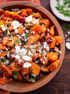 Maple Roasted Carrots in a wooden bowl with feta, dried cranberries and walnuts and a small bowl of parsley to the side.
