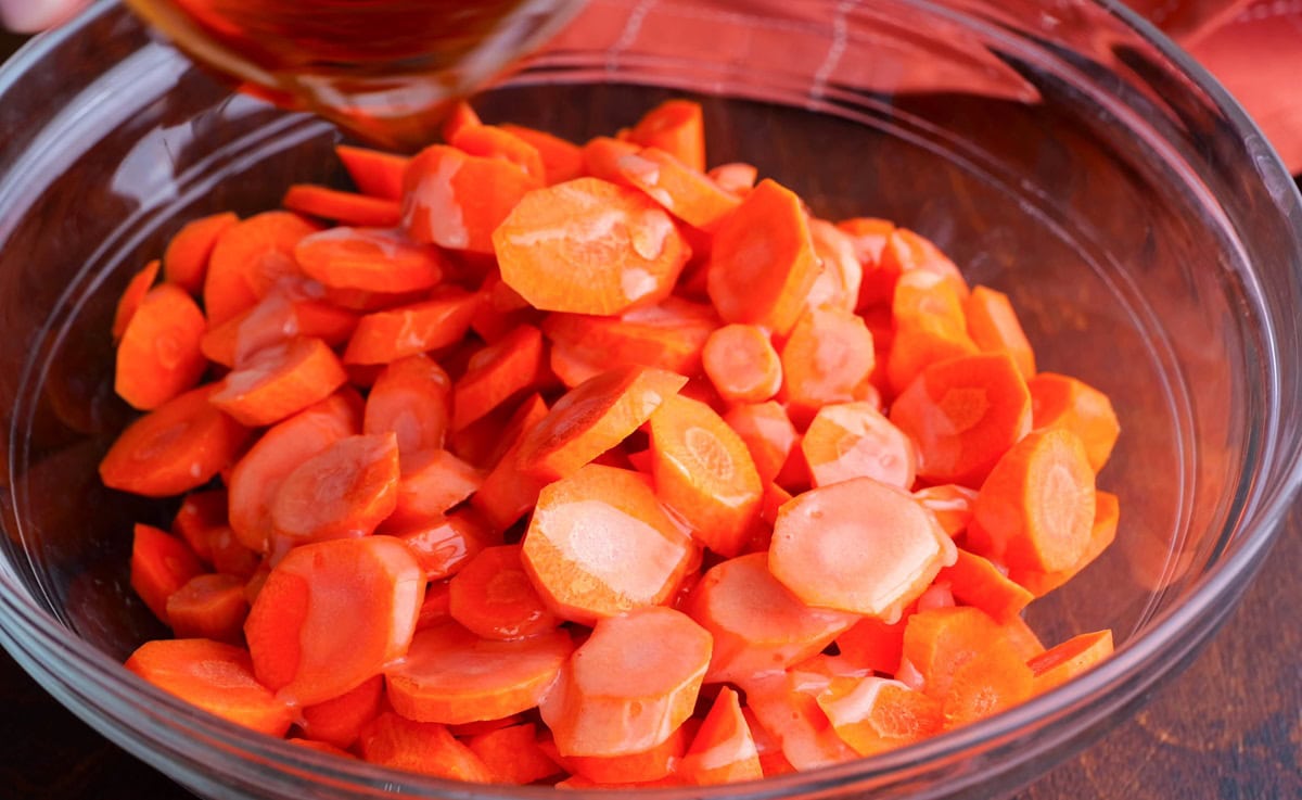 Pouring oil, butter, and pure maple syrup over the raw carrots.