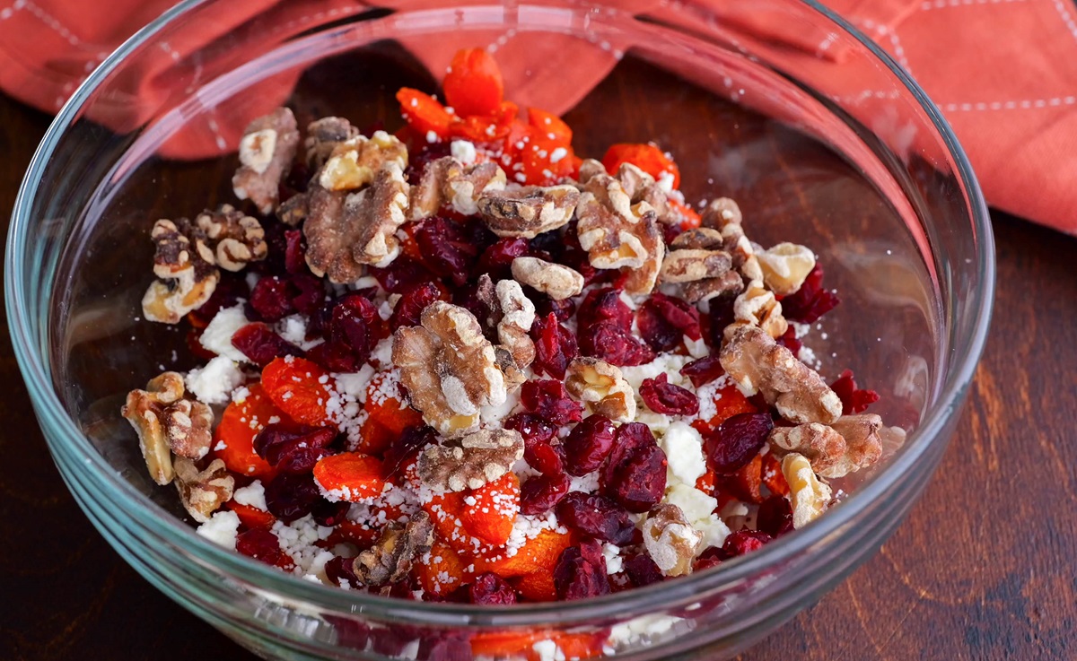 Mixing bowl of carrots, dried cranberries, walnuts, and feta cheese.