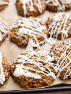 Oatmeal molasses cookies drizzled with melted white chocolate on a baking sheet.