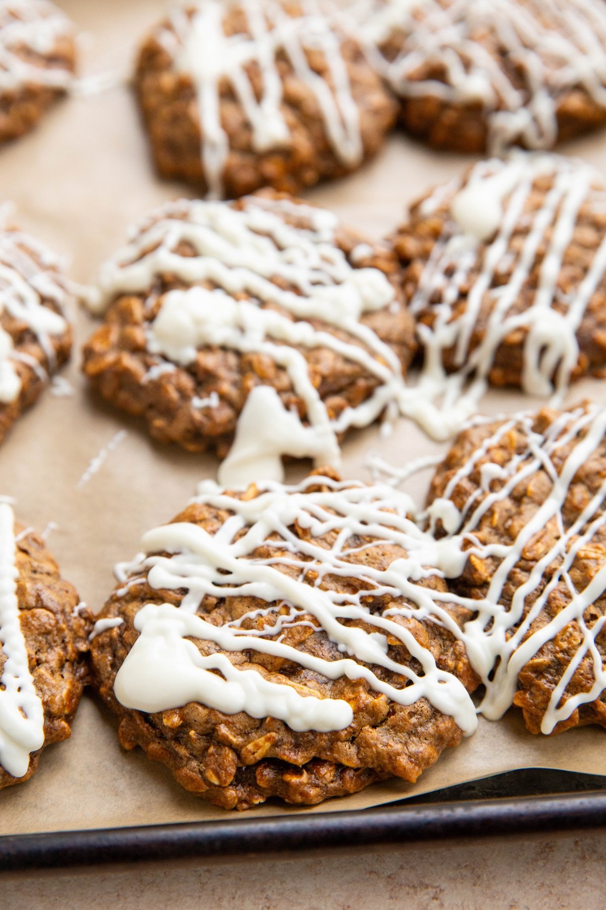 Oatmeal molasses cookies drizzled with melted white chocolate on a baking sheet.