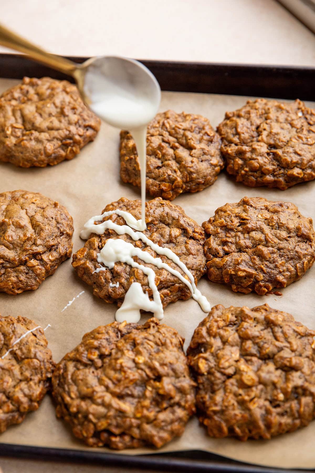 Spoon drizzling white chocolate mixture over chewy ginger molasses cookies.