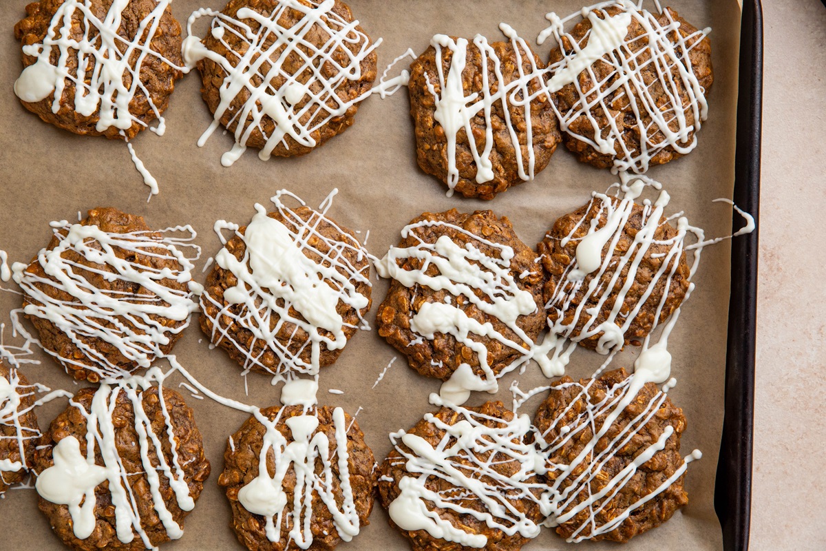 Baking sheet full of oatmeal ginger cookies drizzled with white chocolate.