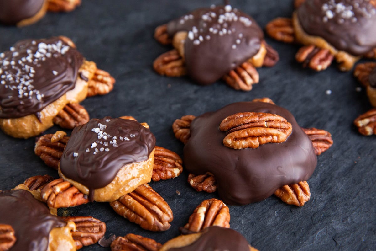 Pecan turtles on a black cutting board, ready to eat.