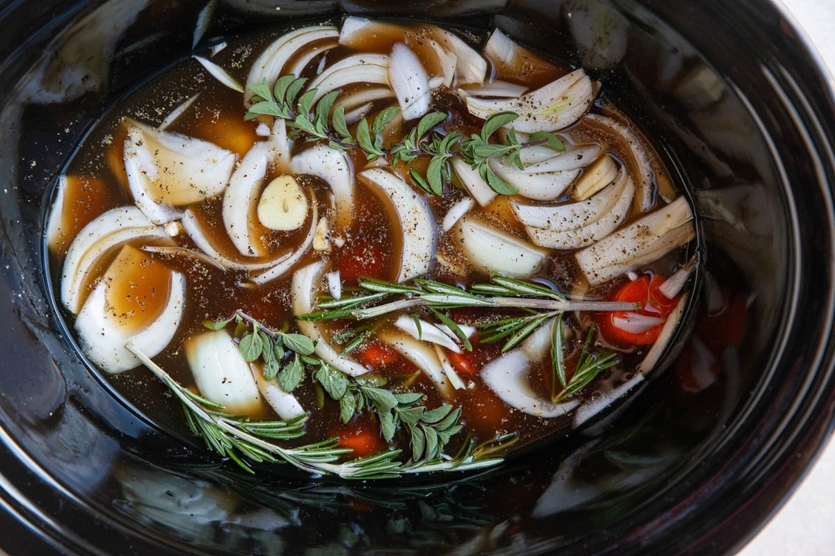 Crock pot with vegetables, fresh herbs, and broth.