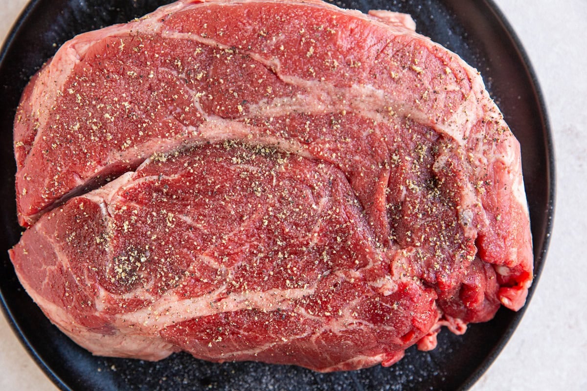 Large chuck roast on a plate seasoned with salt and pepper