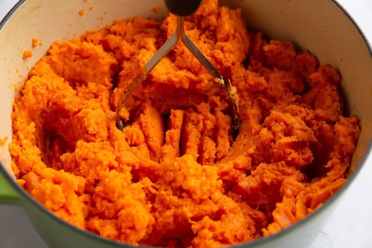 Potato masher mashing sweet potatoes in a large pot.