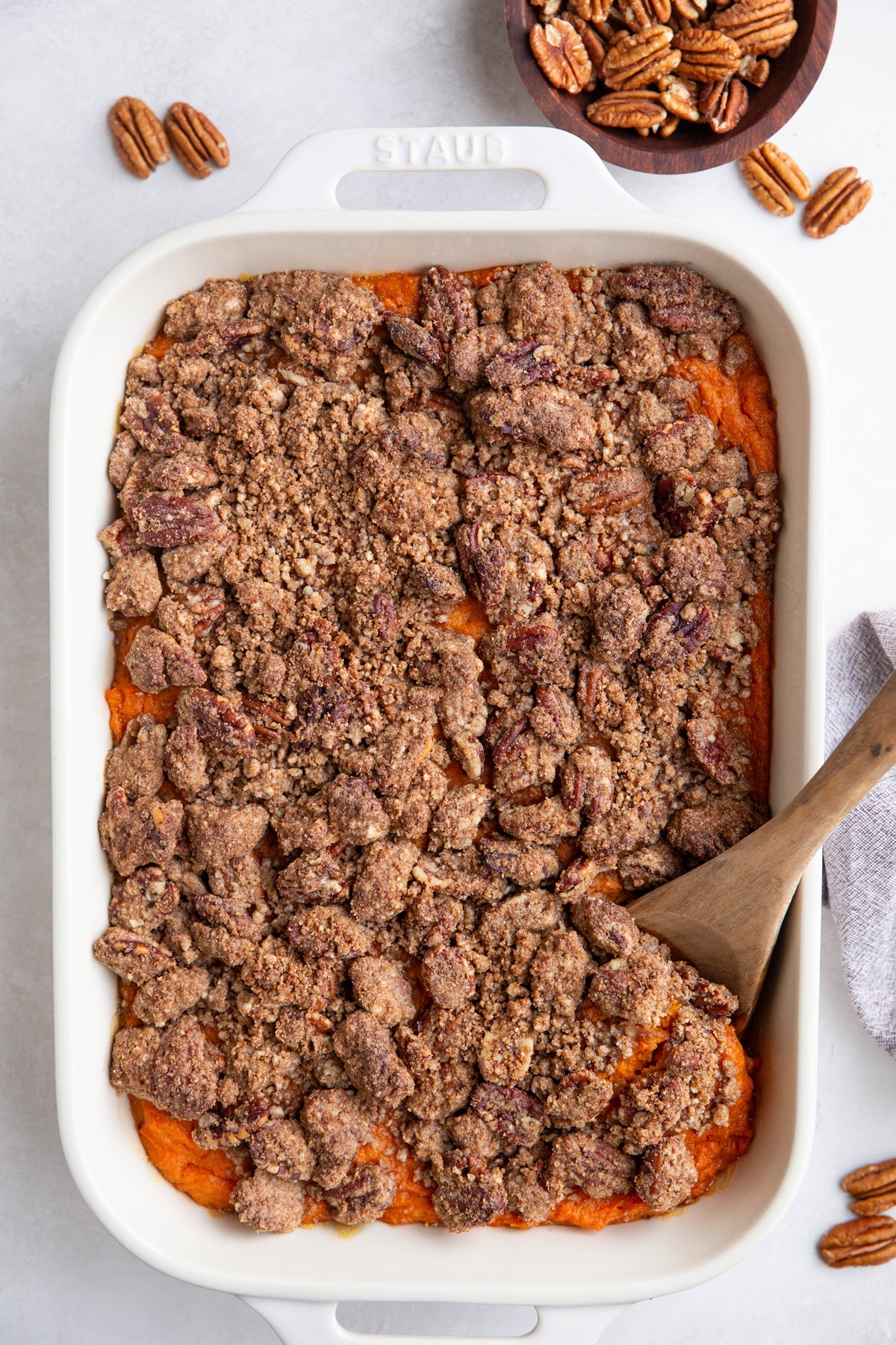 Finished sweet potato casserole on a white backdrop with fresh raw pecans scattered around.