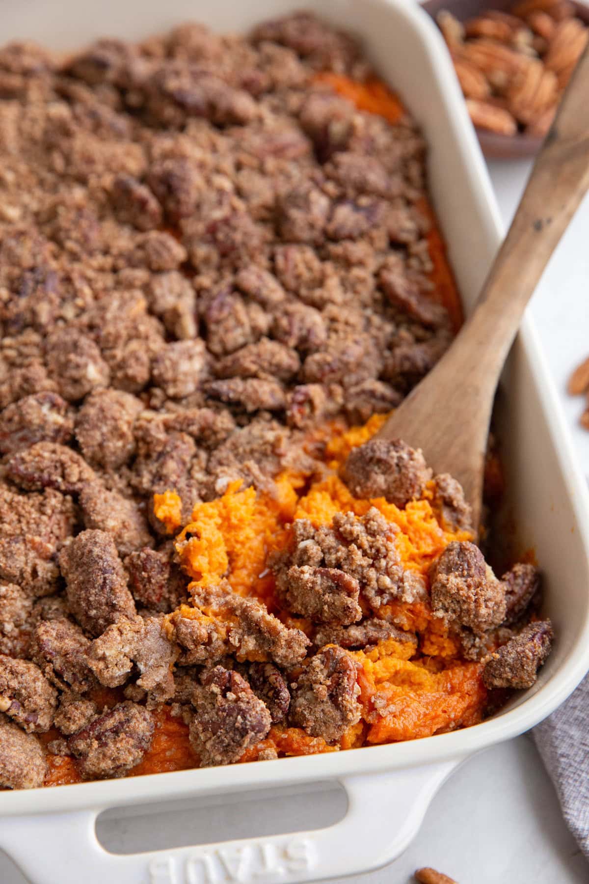 Large white casserole dish of sweet potato casserole with a wooden spoon taking a scoop out.