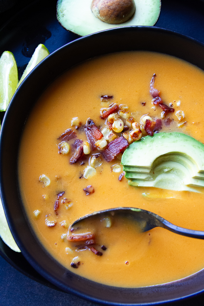 Roasted Butternut Squash and Sweet Potato Soup in a bowl with bacon and avocado on top.