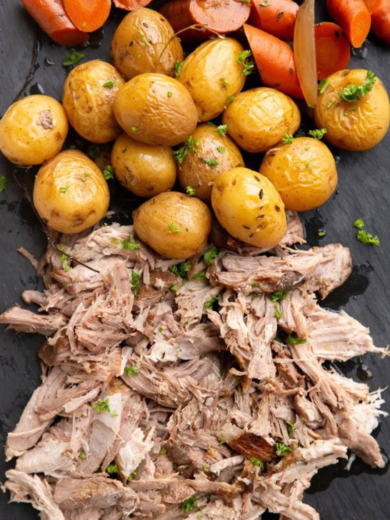 Shredded pork, potatoes, and carrots on a black serving platter.