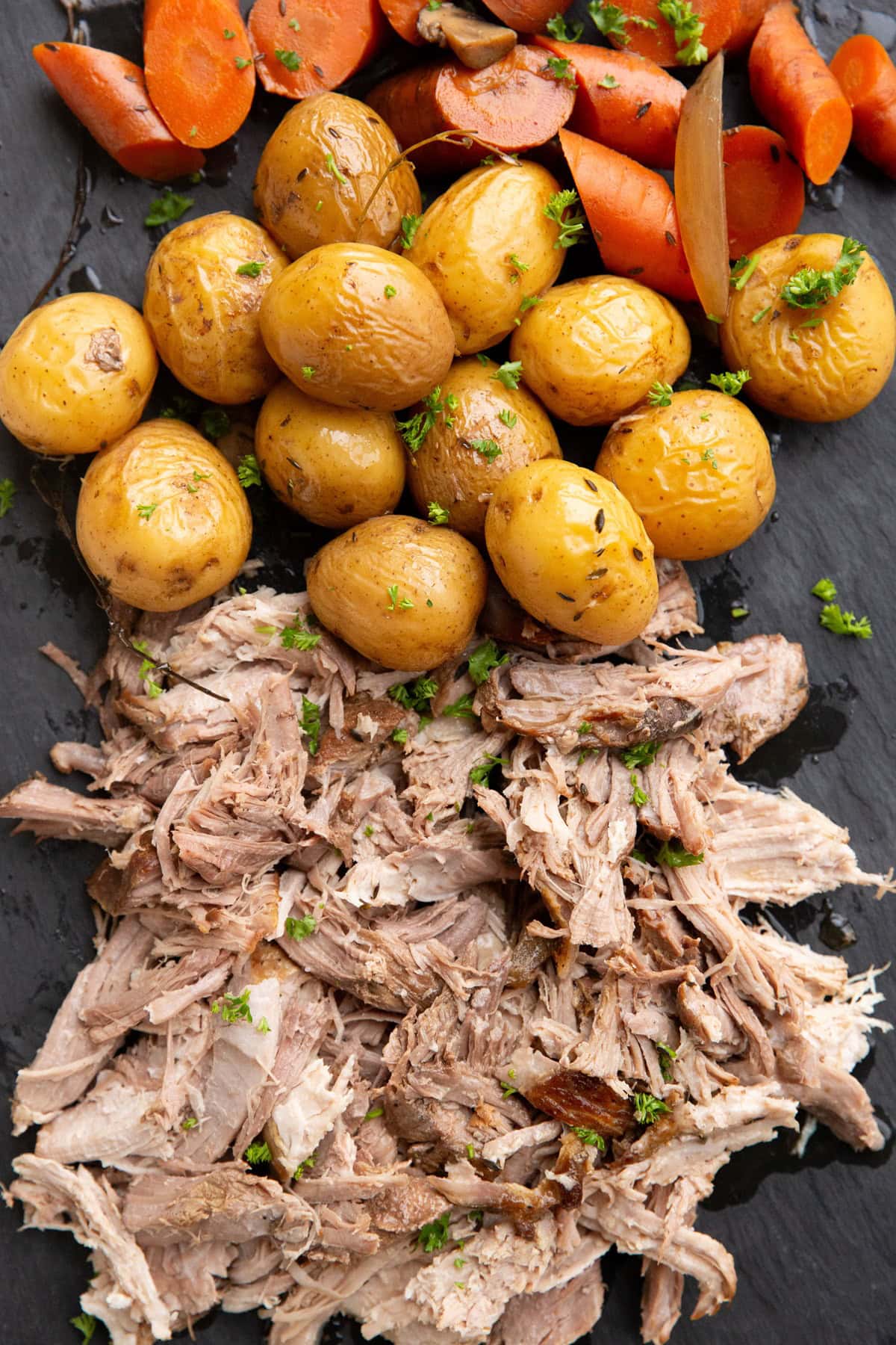 Shredded pork, potatoes, and carrots on a black serving platter.